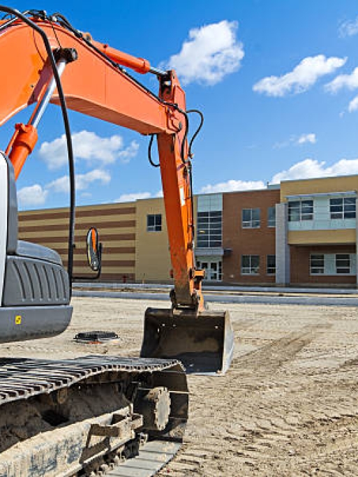 A bright orange construction excavator in the recently graded parking lot of a new high school.Similar Images:
