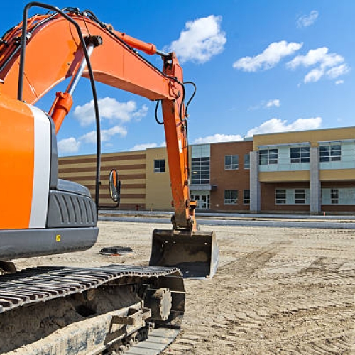 A bright orange construction excavator in the recently graded parking lot of a new high school.Similar Images: